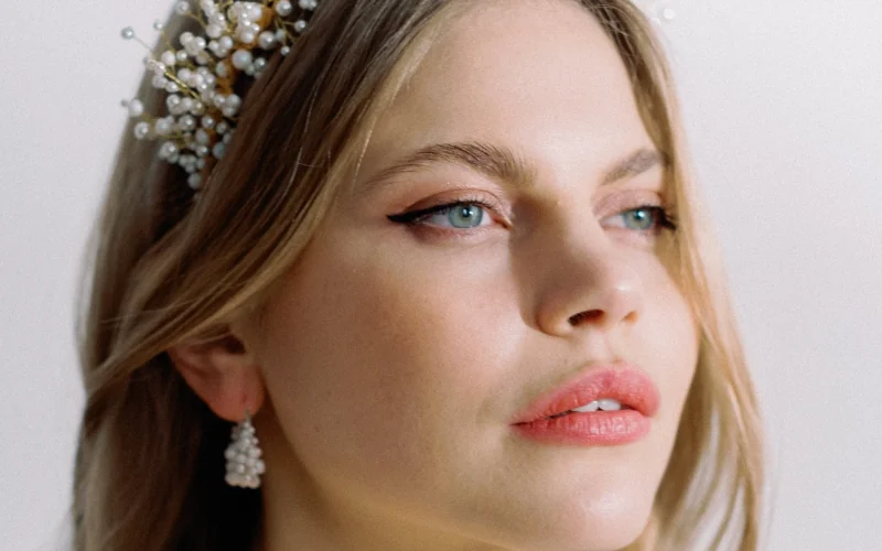 Close up of soft natural bridal makeup with a winged liner, coral lip and a pearl headpiece, shot in flat daylight