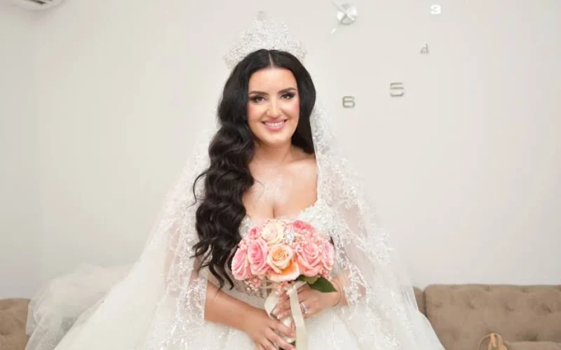 A bride sitting in a bright room in natural light before the ceremony, holding a peach and pink rose bouquet
