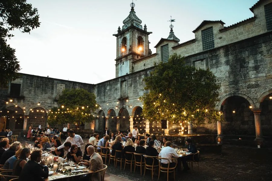 Guests dining in a candlelit courtyard under festoon lights, a Portugal wedding planned by Swish Soirées